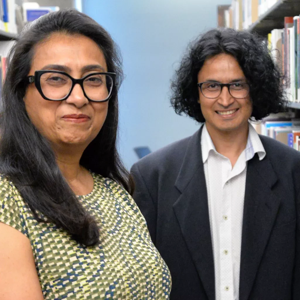 Dr. Asma Sayed and Dr. Pushparaj Acharya stand in a library aisle.