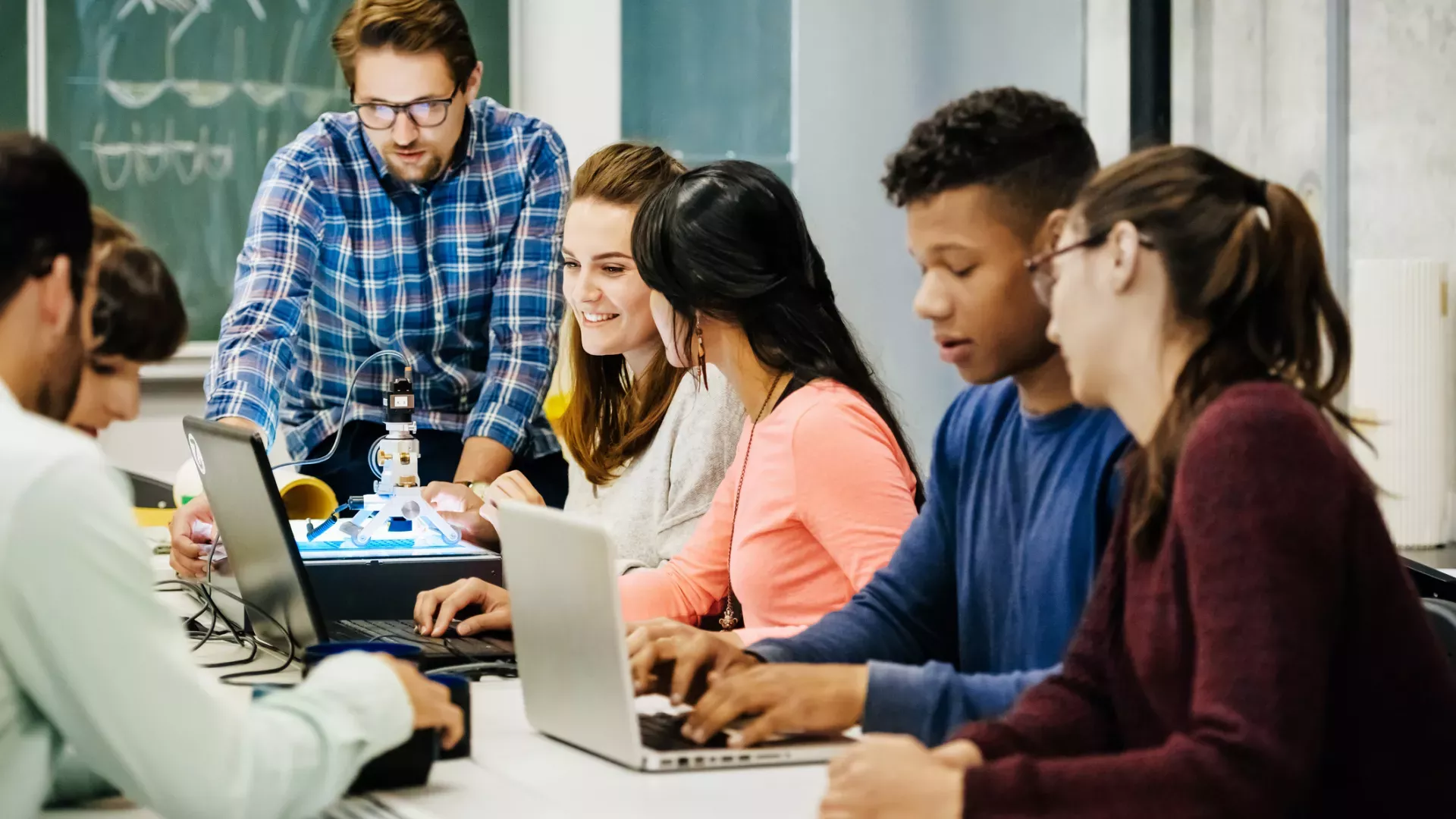 A group of people around a table, working on their laptops and talking